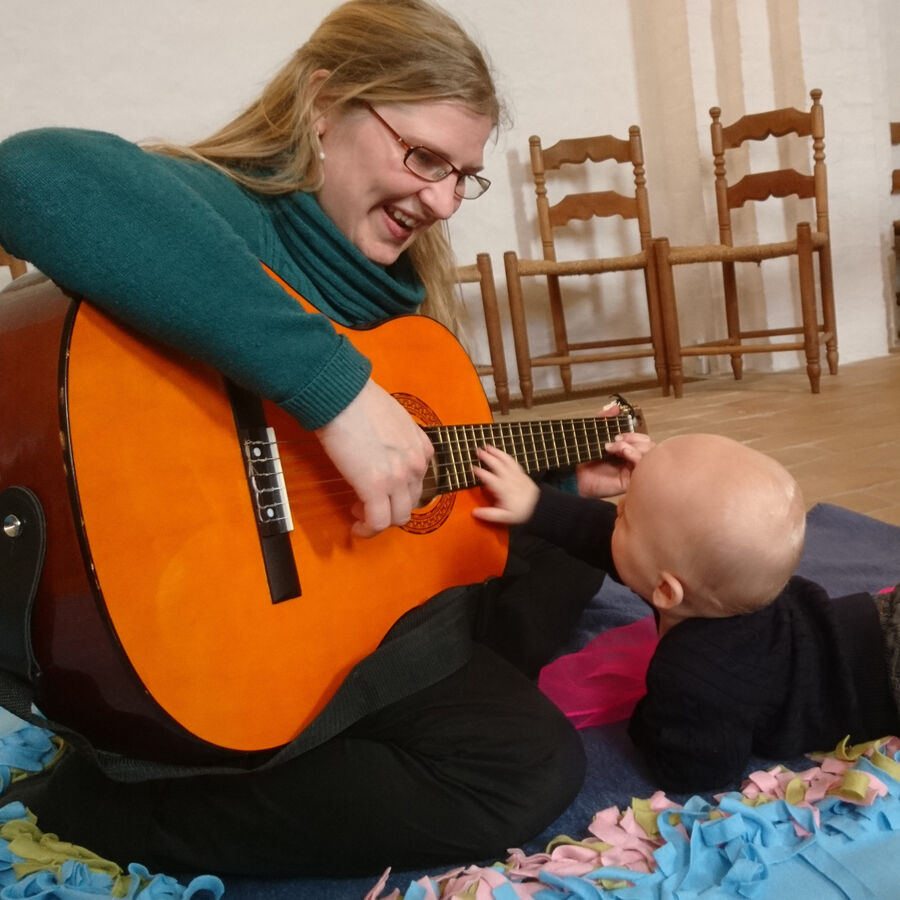 Kvinde spiller på guitar og baby ligger ved siden af